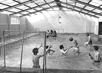 The black and white image shows a group of students playing water polo in the pool at Derwen.