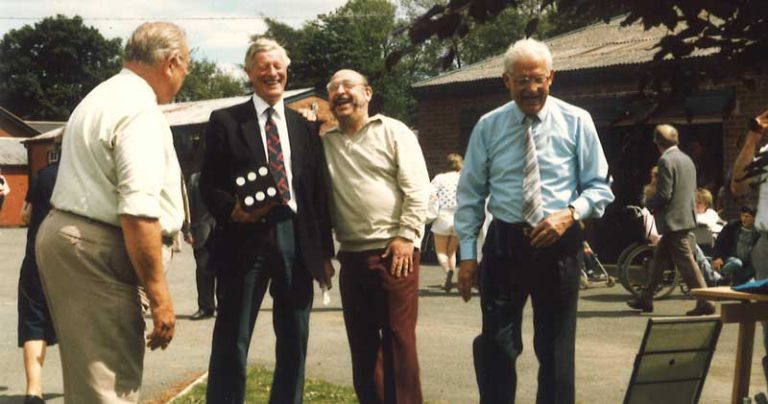Jim Kendall holding large dice at the summer fete, laughing with three other men
