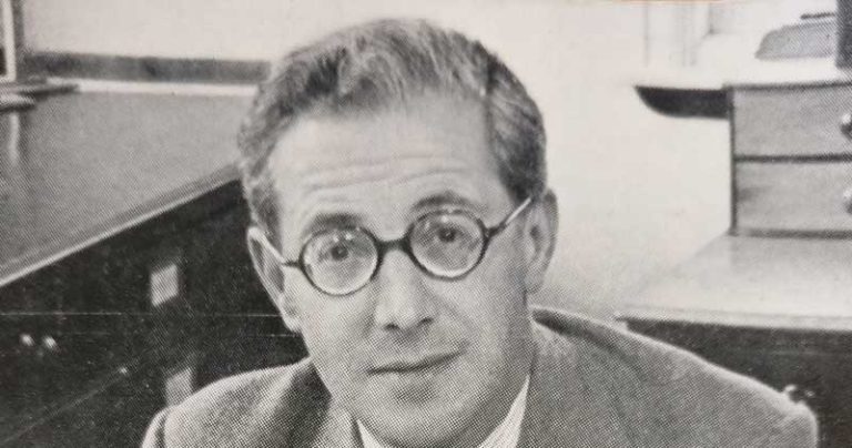 Lord Kenyon looks directly at the camera. The photo is black and white. Lord Kenyon is wearing a suit and has round spectacles.
