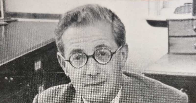 Lord Kenyon looks directly at the camera. The photo is black and white. Lord Kenyon is wearing a suit and has round spectacles.
