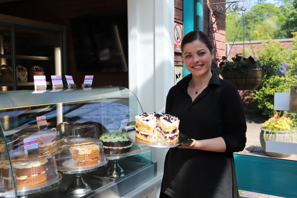 Member of staff from Walled Garden Cafe holding a cake