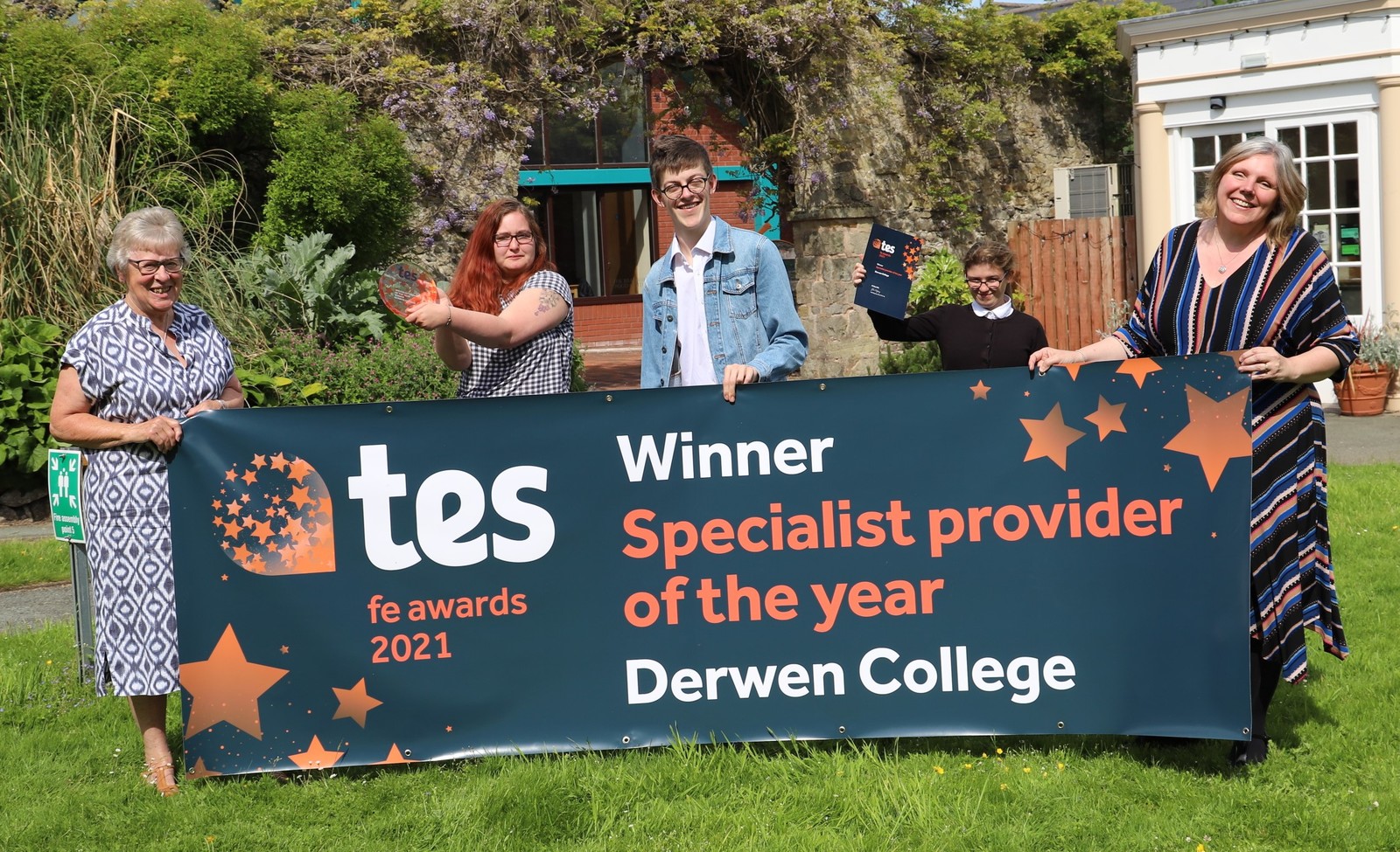 Staff and student hold a banner announcing Derwen College is TES Awards Specialist Provider of the Year