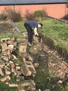 A Derwen College student is clearing rubble from old beds in the Hub Garden as part of his work placement.