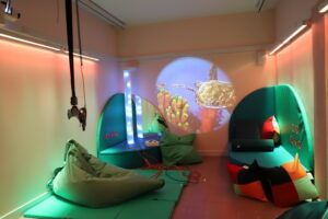 Derwen College Sensory Room with projected sea image on wall, vibrating plinth, light column and beanbag.