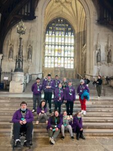 Members of Derwen College Student Union Board, dressed in matching purple Student Union Board hoodies, sitting on the steps outside Westminster.