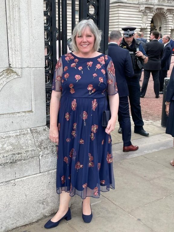 Derwen College principal Meryl Green standing outside Buckingham Palace dressed in a smart navy flowered dress.