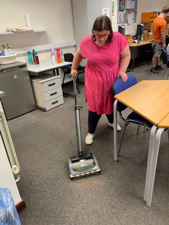 Mia is hoovering at Eco Workshop, practising the independence skills she learnt at Derwen.