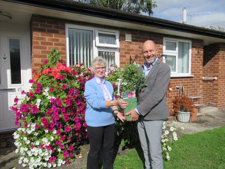 Jackie Tyers, winner of the Best Container category, is presented with a rose by Derwen College Commercial Manager Pete Evans. outside her house with glorious floral pots and planters