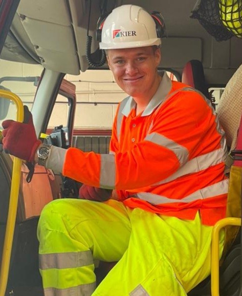 Ben pictured at his full-time job with Kier. Ben wears orange work top and yellow work trousers, and a hard hat.
