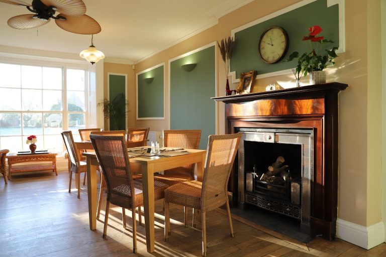 The image shows a view of the inside of the Orangery restaurant. A table with four chairs around it stands in front of a wooden fireplace.