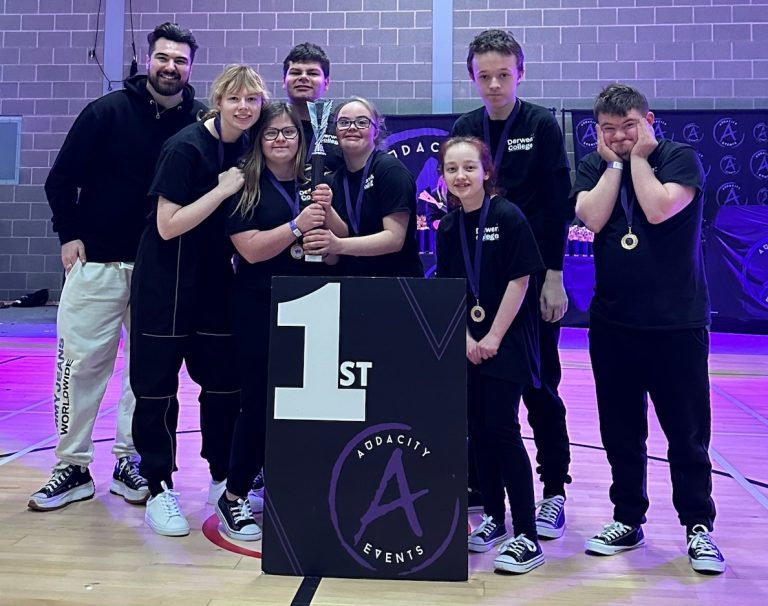 Members of Derwen Dance Crew holding their first place trophy, standing behind a podium with 1st written on it.