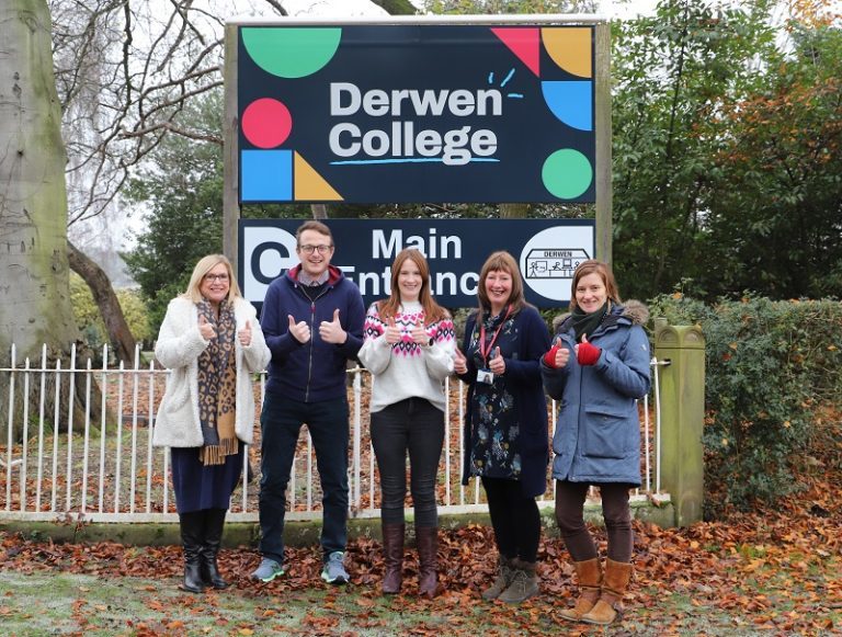 Makaton tutors Paula, James, Lowri, Julie and Helen stand in front of Derwen College's new main entrance sign - which uses a Makaton symbol - all signing the Makaton for 'very good'.