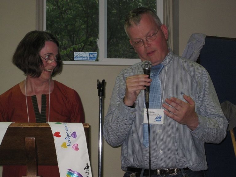 Hazel and Richard stood in front of a lectern and microphone at a pilgrimage for L'Arche Western Canada.