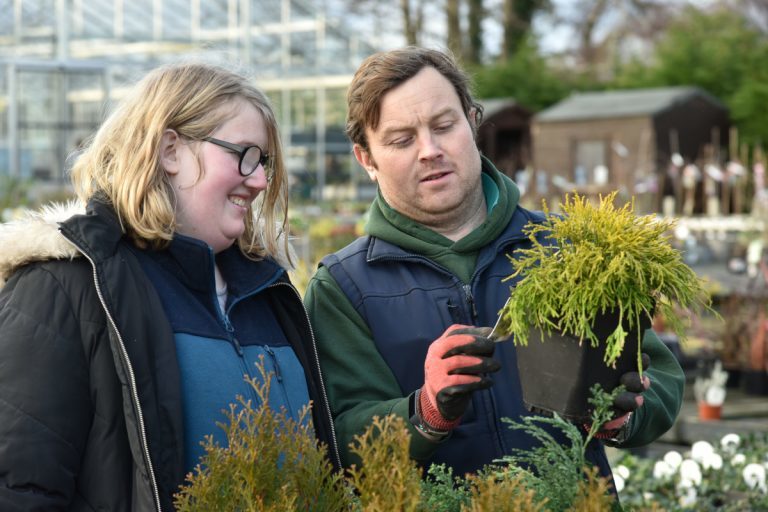 Staff and student looking at a plant in the garden centre.