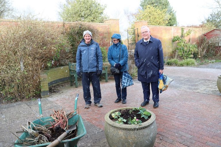 Gardening supervisor Paul Moss, Hazel and Richard stand outside in a snow flurry with the Walled Garden behind them.
