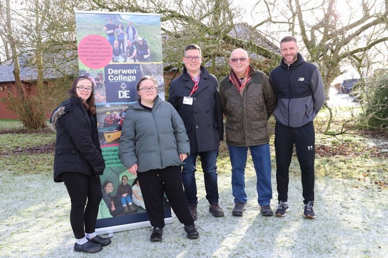 Students Helen Thompson and Anya Bedwell-Garcia, Jamie Chaplin and Steve West-Wynn from Fitz Alan Lodges,and Sports Coordinator Steve Evans stand outside in their coats next to a Derwen Duke of Edinburgh's Award banner.