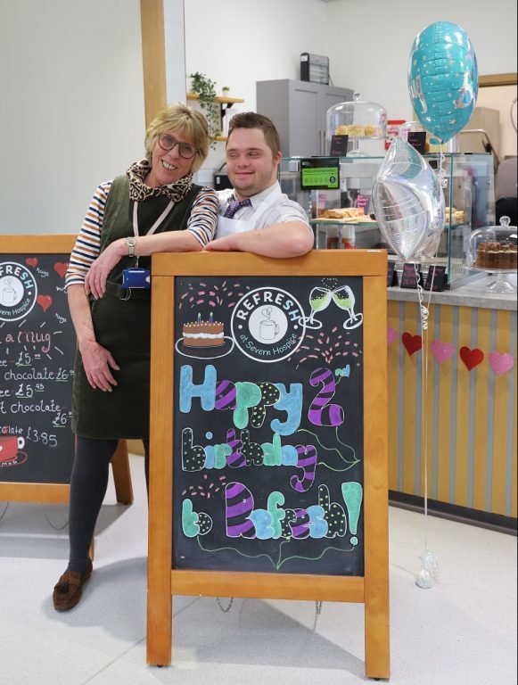 Student George and job coach Gail stand smiling behind Refresh's Happy Birthday board.