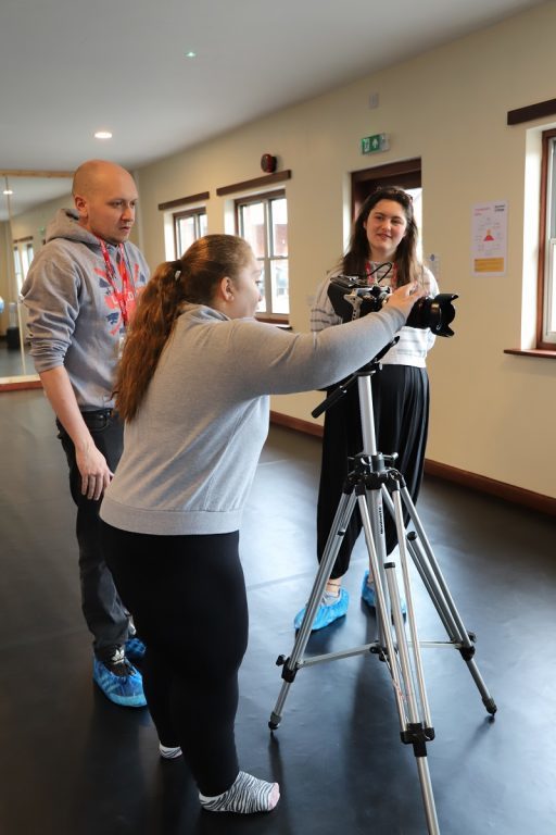 Performing Arts student Izzy adjusts a large video camera on a tripod watched on by Rocking Horse Media producers Gareth and Orla.