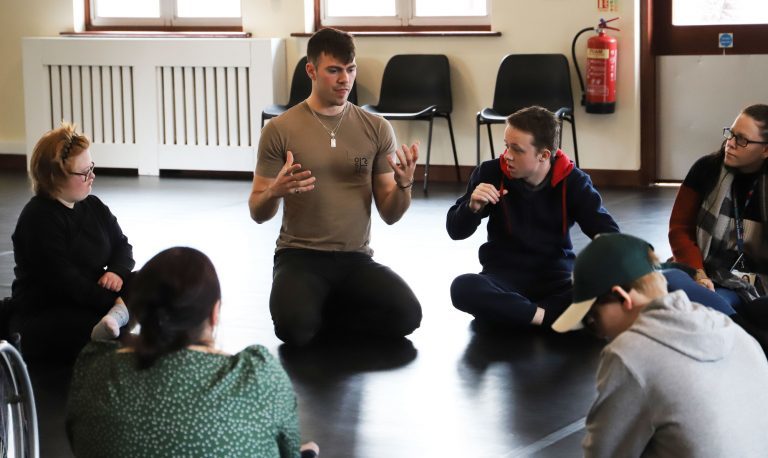 Actor Sam Retford and Performing Arts sat on the floor in a circle as part of a workshop.