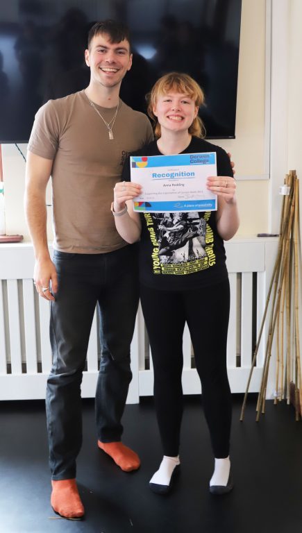 Actor Sam Retford and Performing Arts intern Anna stand together smiling and holding Anna's certificate in recognition of her help with Careers Week.