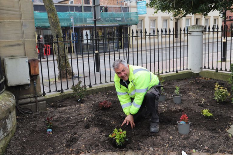 Derwen client Anton (dressed in high-viz jacket) knees down in the border to put a shrub into a hole.