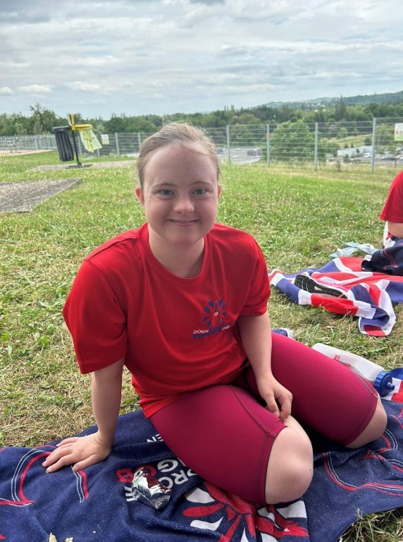 Lizzie, wearing red t-shirt and shorts and sat on a Team GB red, white and blue towel, relaxes between races.