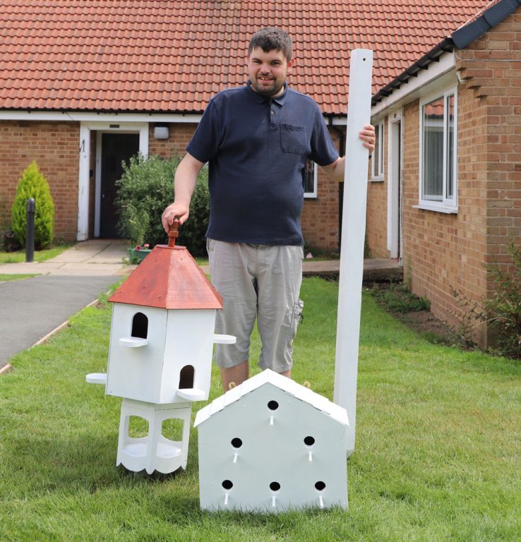Student Mark stands outside his bungalow home with the white painted bird table and dovecote that he has made.