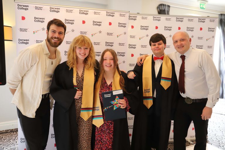 Actor Sam Retford, Performing Arts graduates Anna, Izzy and Josh, wearing black gowns and gold Derwen sashes, and Rocking Horse Media founder Gareth Thomas. All stood in front of large Derwen College banners.