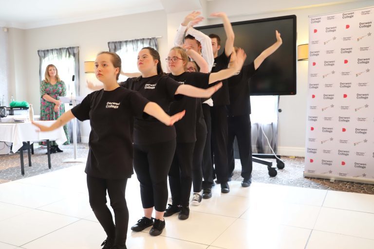 Members of Derwen Dance Crew, dressed in black t-shirts and joggers, stood one in front of the other, with arms held out at different angles.