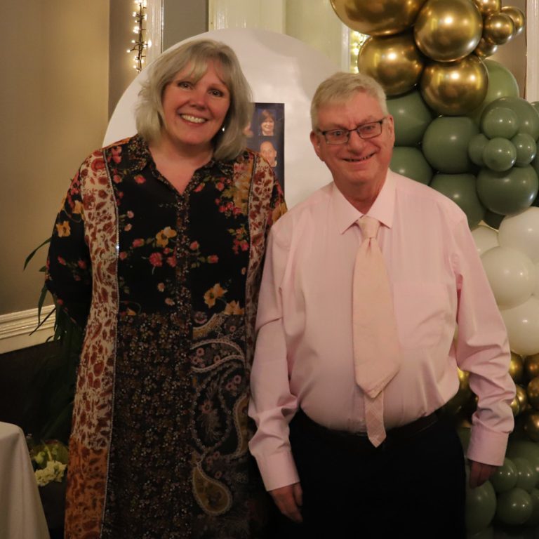 Principal Meryl and long service award winner Alfie smile for the camera, with gold and green balloons behind them.