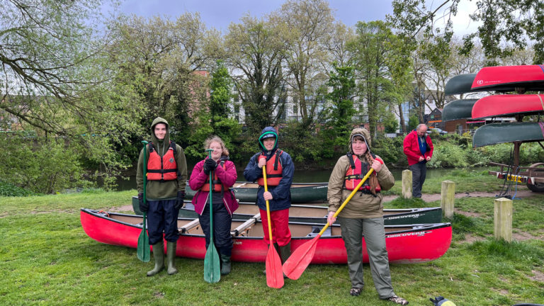 Four people standing next to a canoe