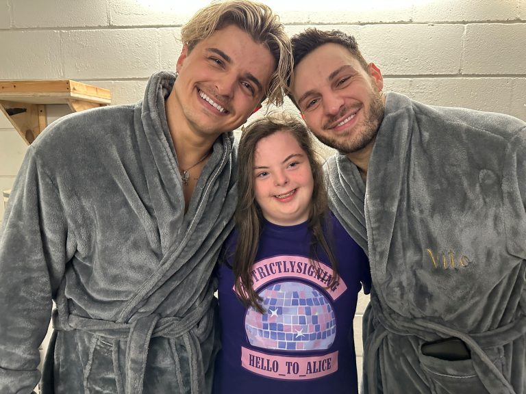 Student Alice, wearing a Strictly t-shirt, with dancers Nikita and Veto wearing grey dressing gowns.
