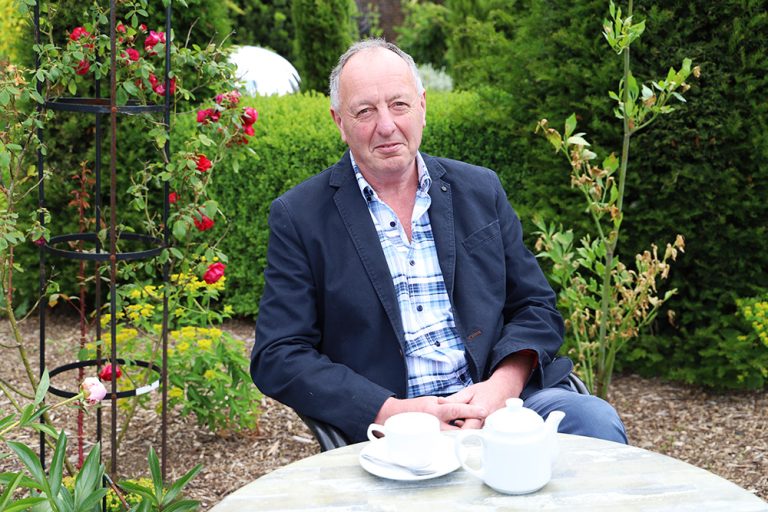 Jamie Ward, Chair of Governors sat in the walled garden at a table with a cup of tea and teapot.