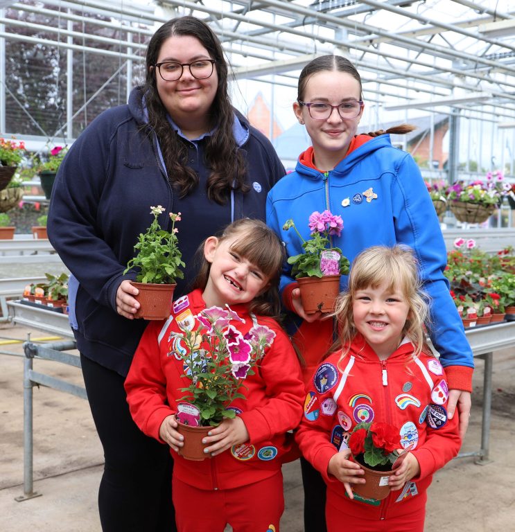 Group photo of guides leader, guide and Rainbows, smiling, wearing hoodies and holding pots of flowers.
