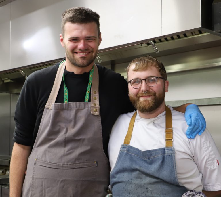 Student Josh stands next to chef Mitch with his arm around his shoulders.
