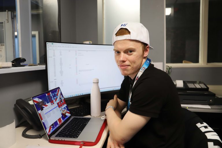 A young man, sat working at his laptop wearing sportswear and a cap