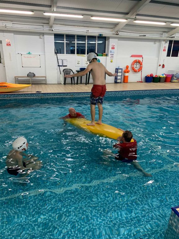 Student standing on a kayak in a swimming pool
