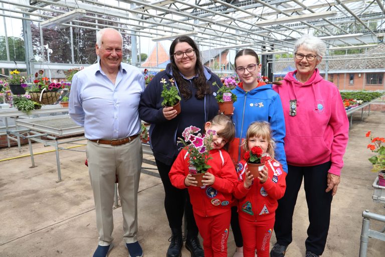 Group photos of Rainbows, guides, guide leaders and Flower & Vegetable Show Chairman Paul, smiling and holding flowers.