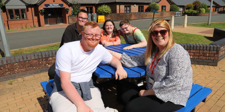 students sit with a member of staff on a blue picnic table