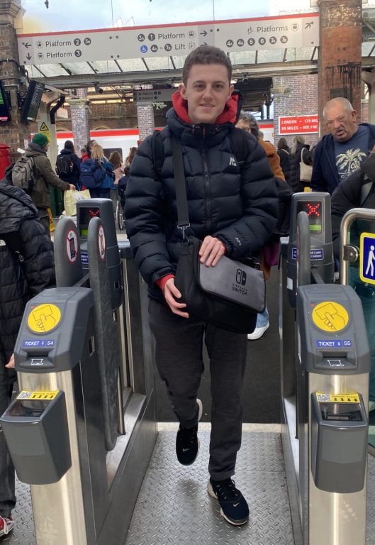 George walking through tickets barrier at station smiling.