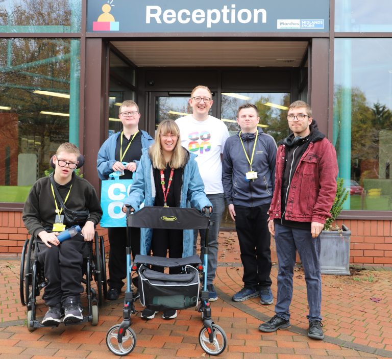Students and Councillor Craig Emery (wearing a Co-op t-shirt) outside Derwen College Reception with one student holding a Co-op bag.