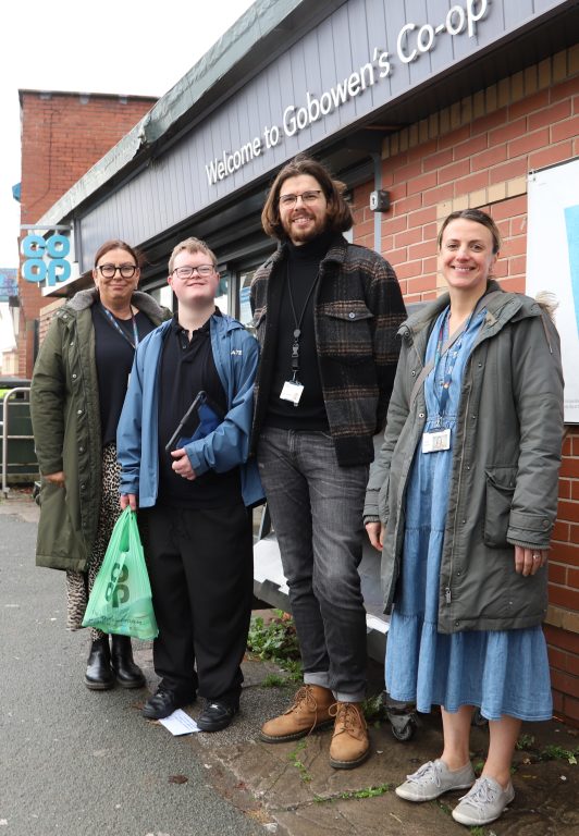 Student and staff members stood outside Co-op, smiling and holding a Co-op bag.
