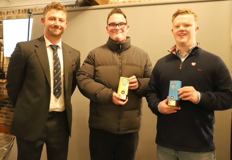 Two students holding an award each, stood with Cricket Shropshire Inclusion Officer Tyler who is wearing a smart suit and cricket tie.