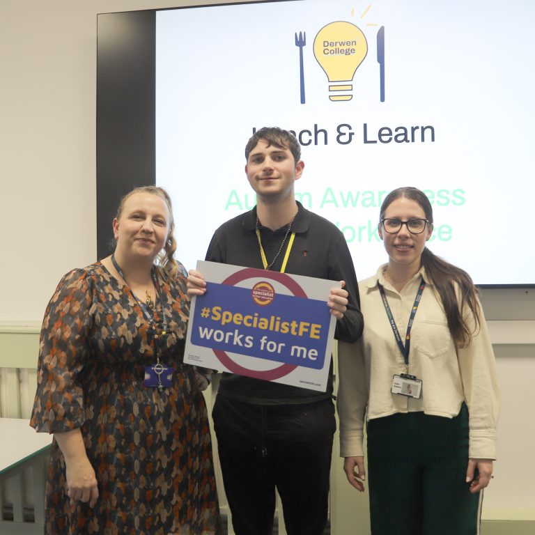 Two female staff members and student Byron stand in front of the Lunch and Learn slide, with Byron holding a sign which says #specialistFeworksforme