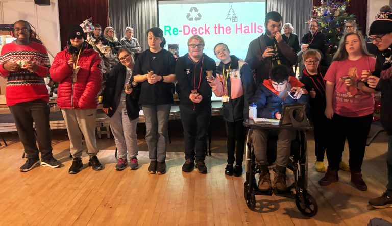 group of student representatives holding their mini Christmas tree prizes stood in front of a screen with Re-Deck the Halls on it and a Christmas tree.