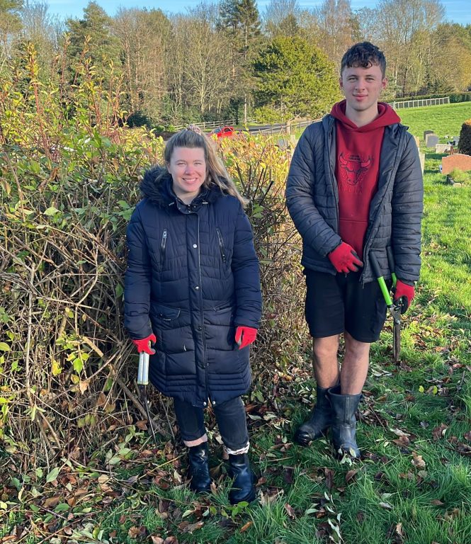 Teacher Maddie in a warm coat, boots and gloves with student Ben in hoodie and shorts and gloves. Both holding shears.
