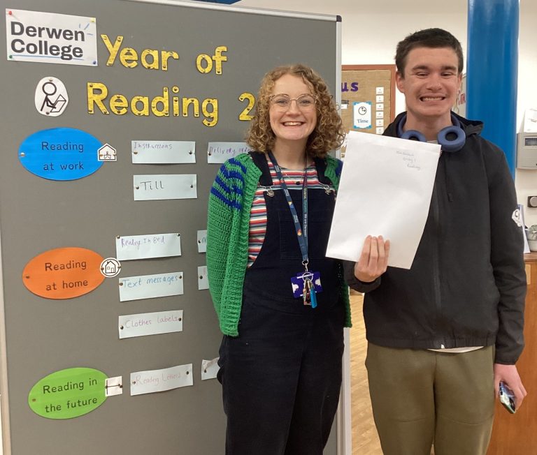 Teacher and student - holding a piece of paper - smiling proudly in front of a Year of Reading 2026 display board.