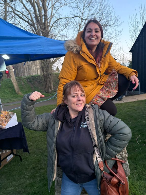 Woman wearing Derwen College hoodie doing strong muscle pose with smiling fundraising coordinator behind, both smiling.