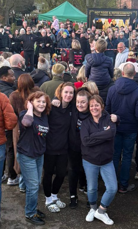 Four staff members dresses in Derwen Charity branded t-shirts and hoodies stood in front of crowds of people and stalls at whittington Castle.