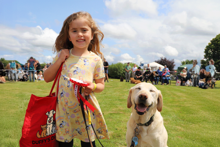 Young girl holding dog show rosette and Duffy's Diner bag along with her happy looking golden labrador type dog